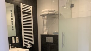 Un baño moderno con ducha de vidrio, lavamanos blanco, inodoro y barra para toallas.