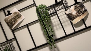 Una pared con una celosía metálica negra, dos fotografías blanco y negro, y una planta verde.