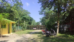 A dirt path leading to a building with a green roof, surrounded by trees and a parked motorcycle. - Homocation Sikhiri Cottages (Barnagar)