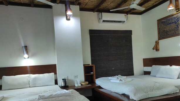 A hotel room with two beds, a coffee maker, a basket, and a wall-mounted air conditioner. - Homocation Sikhiri Cottages (Barnagar)