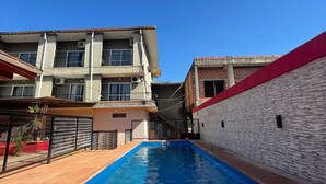 Una piscina con solárium empedrado, rodeada de edificios con balcones y techo rojo.
