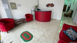 Zona de recepción con un escritorio rojo, una silla roja, un banco y un tapete rojo y verde sobre un suelo de baldosas.