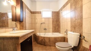 Een badkamer met een wastafel, toilet, badkuip en een raam boven de badkuip.