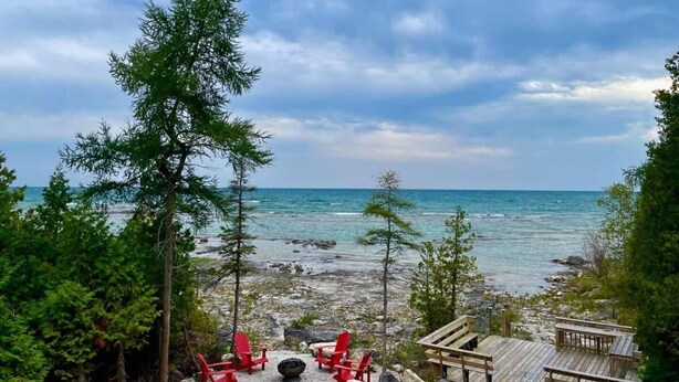 Vista sulla spiaggia con una veranda in legno, sedie rosse e un litorale roccioso.