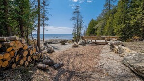 Un ambiente naturale con una terrazza in legno, tronchi e una spiaggia rocciosa.
