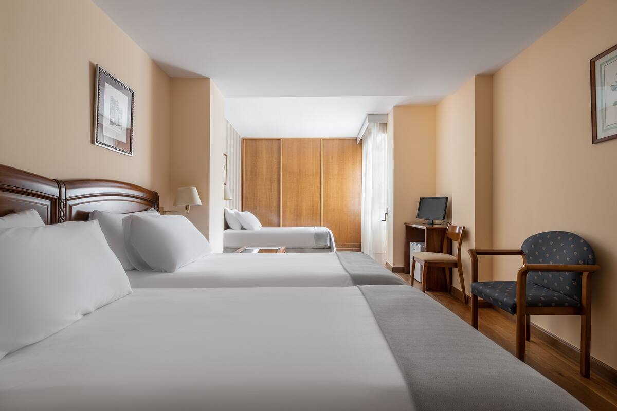 A hotel room with two beds, a desk, a chair, and a wardrobe.