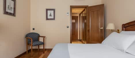 Una habitación de hotel con una cama, una silla, una lámpara y una puerta que da a otra estancia.