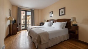 Habitación de hotel con dos camas, un balcón y vistas a edificios.