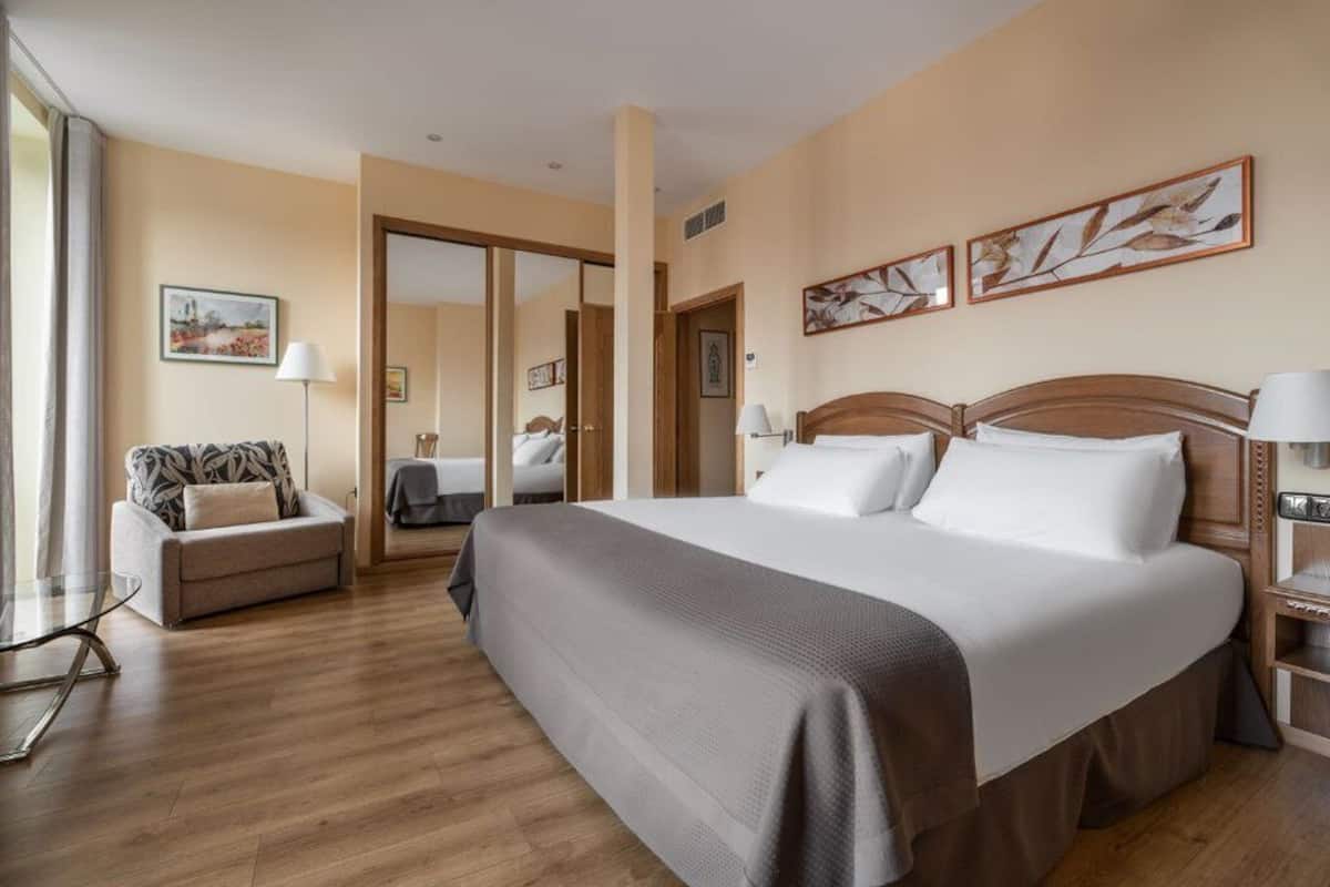 A hotel room with a large bed, a sofa, a desk, and a mirror.
