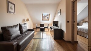 Una habitación moderna y luminosa con un sofá de cuero marrón, una mesa de centro de vidrio, un escritorio con una computadora y una cama.