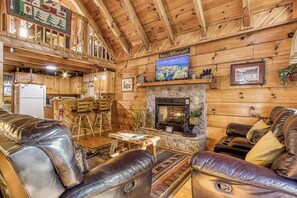 A log cabin interior with a stone fireplace, leather sofas, a dining area, and a kitchen. - This spectacular 2 bedroom, 2 bath Smoky Mountain log cabin offers the perfect getaway! (Sevierville)