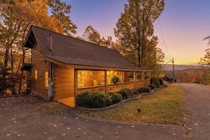 A wooden cabin with a porch, surrounded by trees and a clear sky. - This spectacular 2 bedroom, 2 bath Smoky Mountain log cabin offers the perfect getaway! (Sevierville)