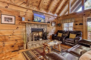 A log cabin interior with a stone fireplace, leather furniture, and a television mounted above the fireplace. - This spectacular 2 bedroom, 2 bath Smoky Mountain log cabin offers the perfect getaway! (Sevierville)