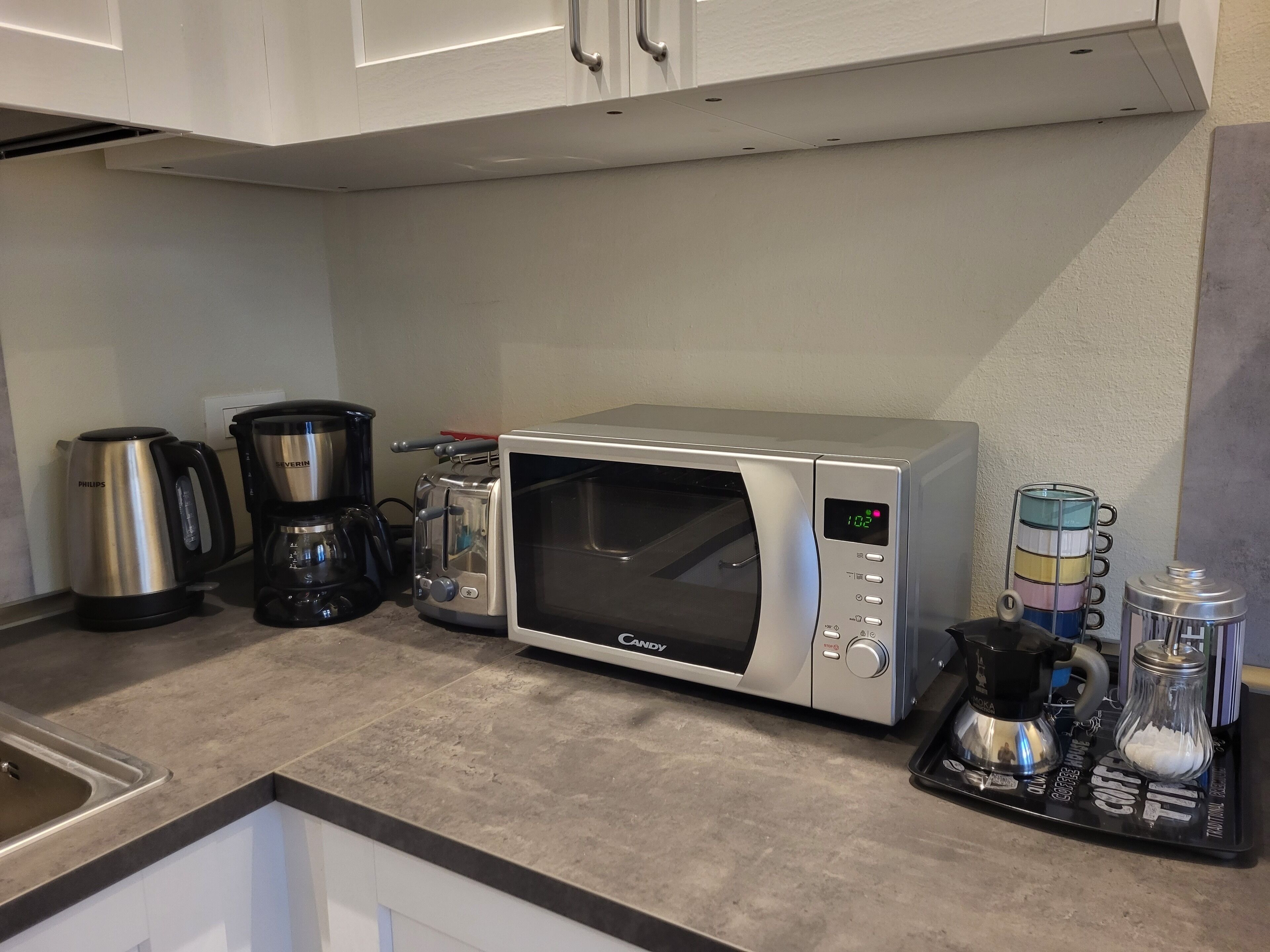A kitchen with a microwave, coffee maker, and a coffee grinder.