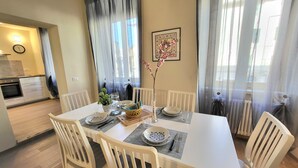 A dining area with a white table set for four, surrounded by white chairs. A small kitchen is visible in the background. - LO STELLARIO DI LUCCA in the historic center, parking very close, WiFi (Lucca)