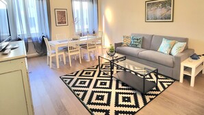 A modern living room with a grey sofa, a coffee table, and a dining area with white chairs and a table. - LO STELLARIO DI LUCCA in the historic center, parking very close, WiFi (Lucca)