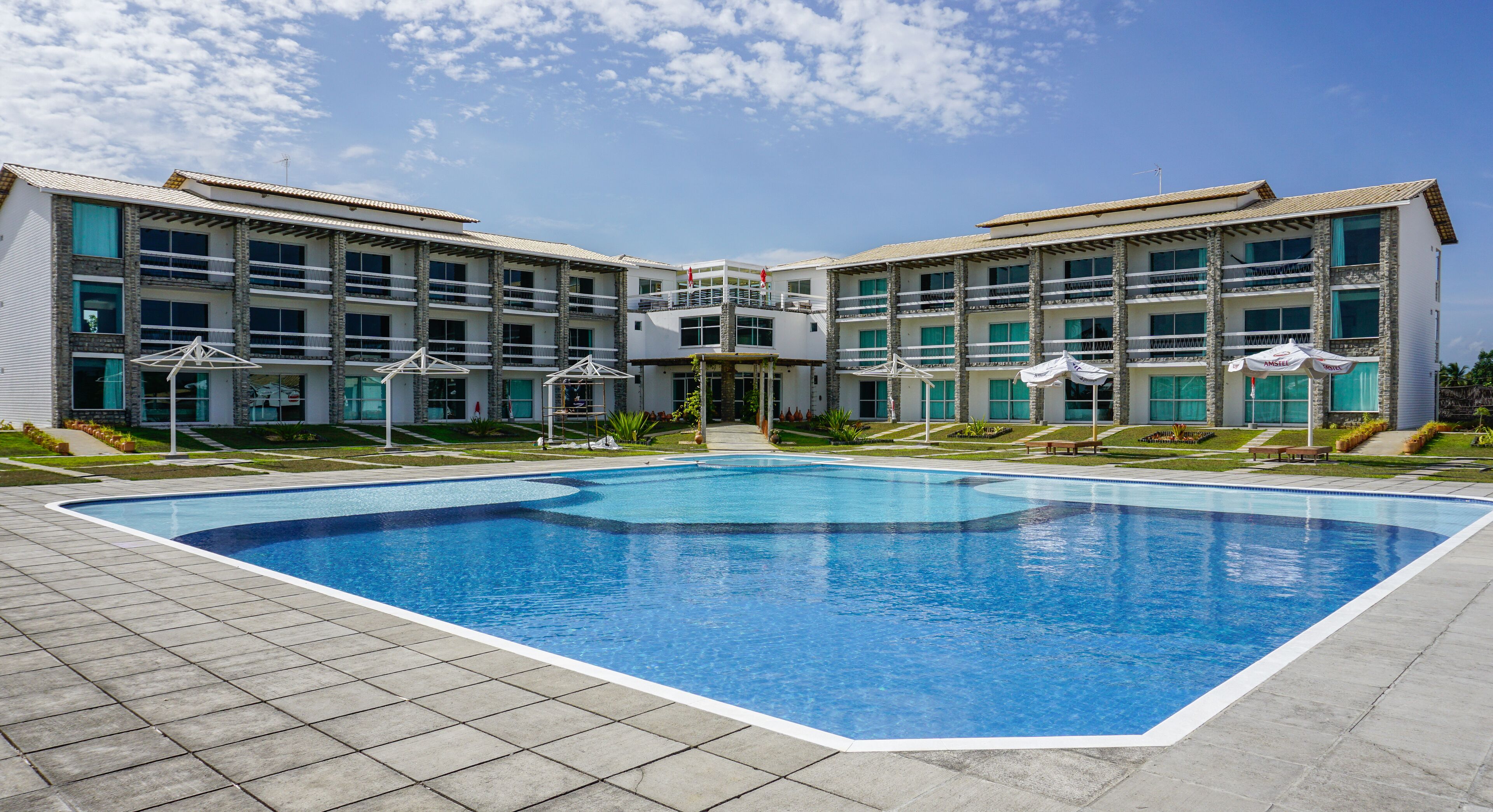 A modern hotel with a large swimming pool, multiple balconies, and outdoor seating areas.
