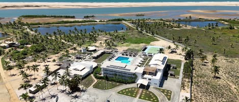 An aerial view of a resort with a swimming pool, tennis court, and beachfront access.