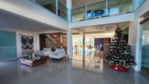 Un interior espacioso y moderno con techo alto, balcón con barandilla de vidrio y un árbol de Navidad.