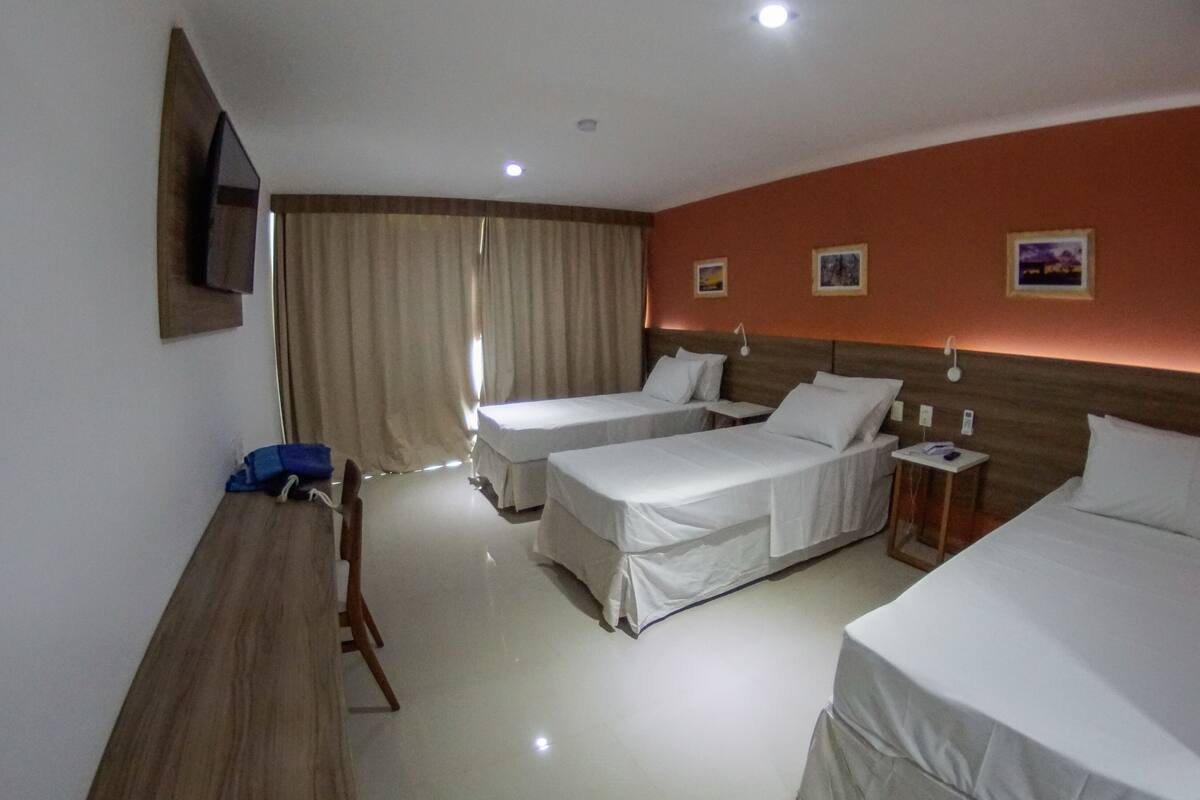 Een hotelkamer met twee eenpersoonsbedden, een bureau, een stoel, een aan de muur bevestigde televisie en een raam met gordijnen.