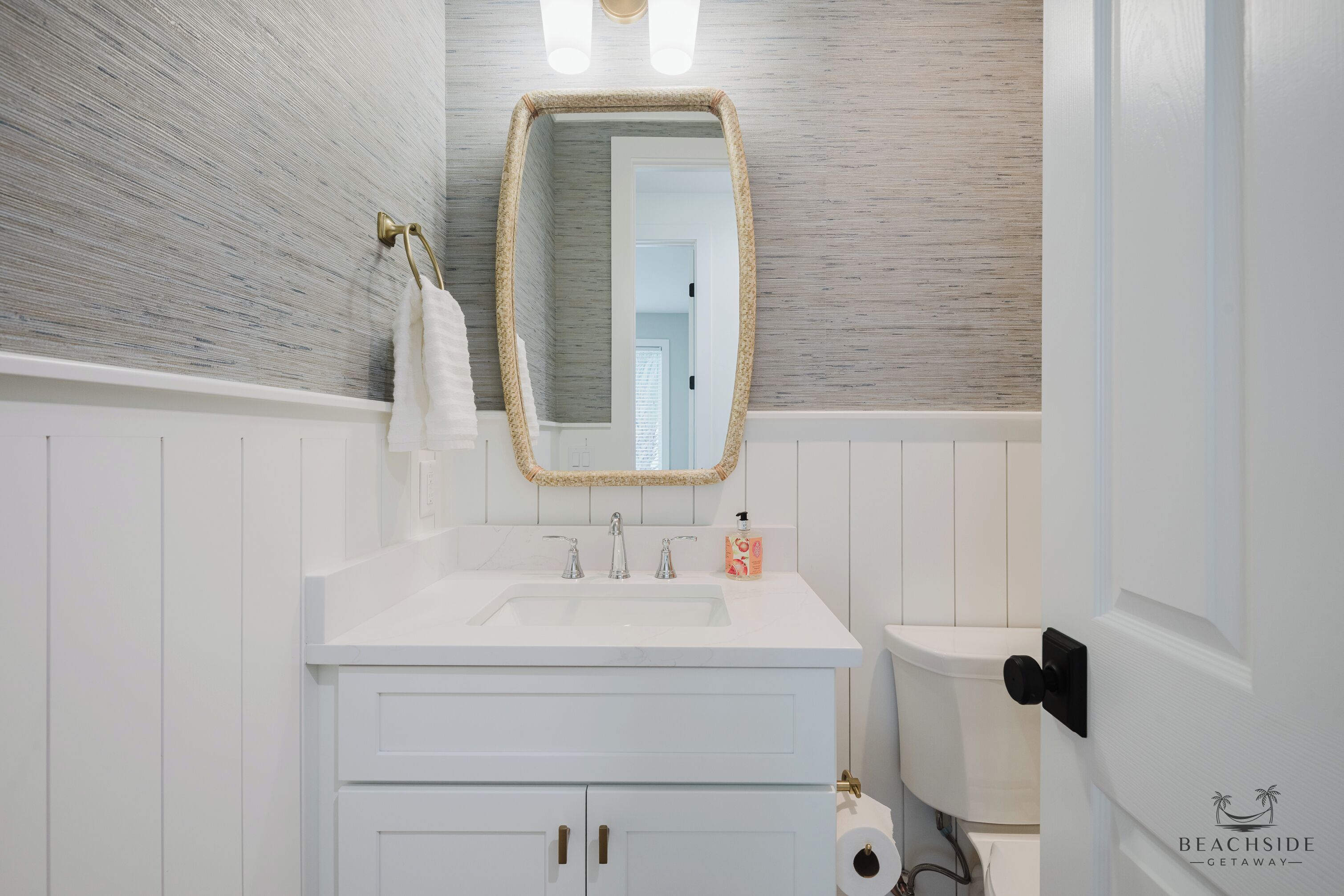 Une salle de bain avec un meuble-lavabo blanc, un miroir avec un cadre doré, des toilettes et une serviette accrochée au mur.