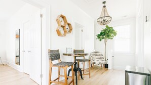 Un espace repas lumineux et moderne, avec une table ronde et deux chaises, une étagère hexagonale en bois, un luminaire suspendu et une plante en pot.