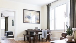 Ein modernes Wohnzimmer mit Essbereich, einem großen Fenster mit Vorhängen, einem Stadtbildgemälde und einem Bett im Hintergrund.