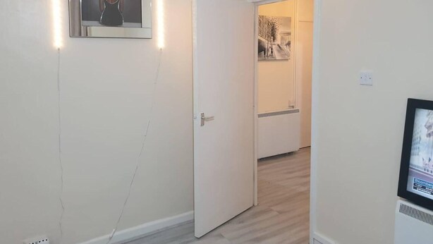 A hallway with a white door, a framed picture on the wall, and a television screen displaying a news channel.