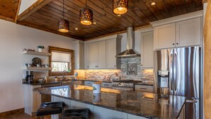 Una cocina moderna con encimeras de granito, electrodomésticos de acero inoxidable y una isla central con taburetes de bar.