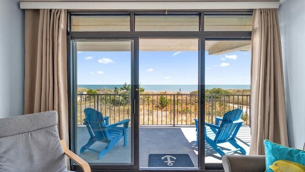 A balcony with a view of the beach, two blue chairs, and a grey sofa.