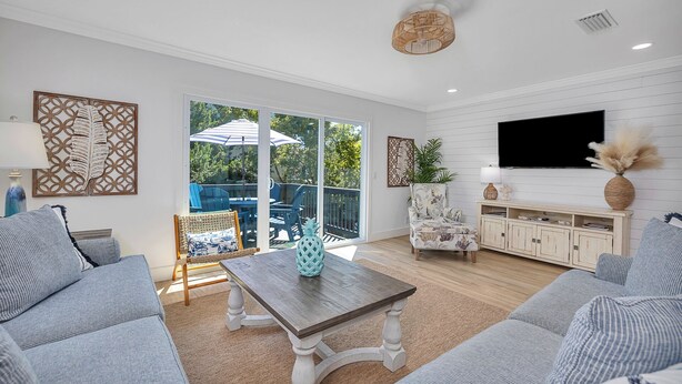 A spacious living room with a large sliding glass door leading to an outdoor patio, a wooden coffee table, and a TV mounted on the wall.