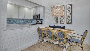 A modern kitchen with white cabinetry, a microwave, and an oven. There is a dining area with a wooden table and wicker chairs.