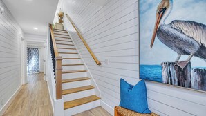 A staircase with wooden steps and a handrail, leading to a room with a woven bench and a large pelican painting on the wall.