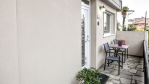 Een klein terras buiten met een tafel, stoelen, een plant in pot en een deur naar een berging.