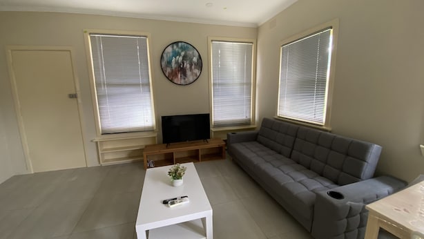 Un salon avec un canapé gris, une table basse blanche, un téléviseur à écran plat posé sur un meuble en bois et un tableau accroché au mur.