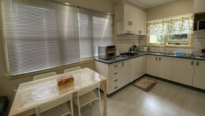 Une cuisine moderne avec des meubles blancs, une cuisinière à gaz, un four à micro-ondes et une fenêtre équipée de stores.
