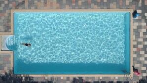 Vista aérea de una piscina rectangular con agua cristalina, rodeada por una solana con baldosas.