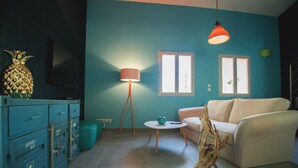 Una sala de estar con una pared verde azulado, un sofá blanco, una mesa de centro y otra mesa de centro de madera. Hay una piña en la encimera y una lámpara en una esquina.