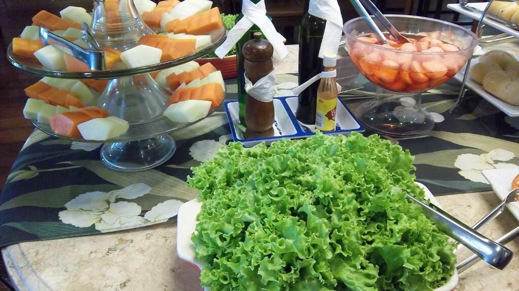 A buffet table with various food items including a large bowl of lettuce, a glass bowl of sliced fruit, and a glass dish with cubed cheese.