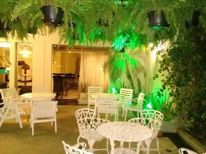 An outdoor seating area with white chairs and tables, surrounded by lush greenery and artificial plants. - Canoas Parque Hotel (Canoas)