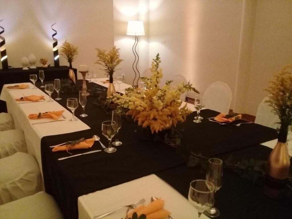 Et spiseområde med borde dækket til et måltid, hvide duge, pænt anrettet bestik og blomsterarrangementer i midten.