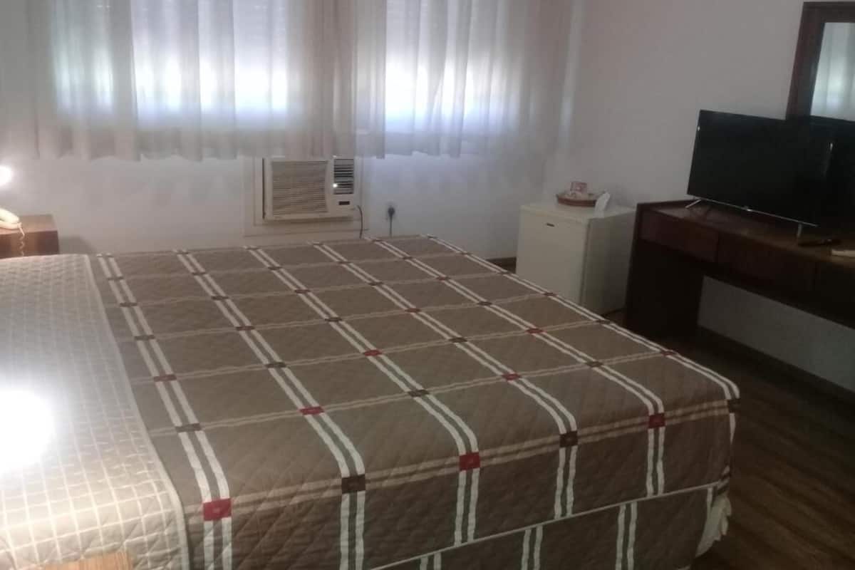 Ein Hotelzimmer mit Bett, Fernseher, Schreibtisch und einem kleinen Schrank.