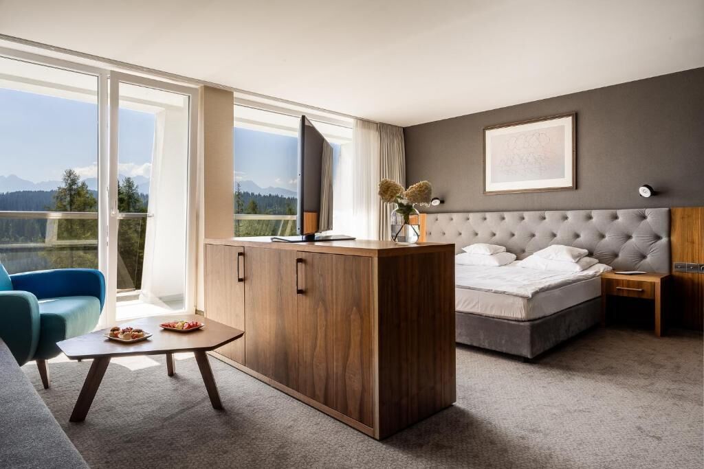 Un dormitorio con cama, un escritorio de madera, una silla, una mesita de noche y un ventanal con vistas.