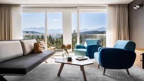 Una sala de estar moderna con un sofá, sillones, una mesa de centro y vistas a montañas a través de amplios ventanales.