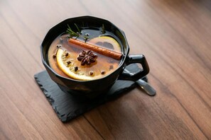 Una taza de bebida caliente con rodajas de limón, anís estrellado y canela sobre una mesa de madera.
