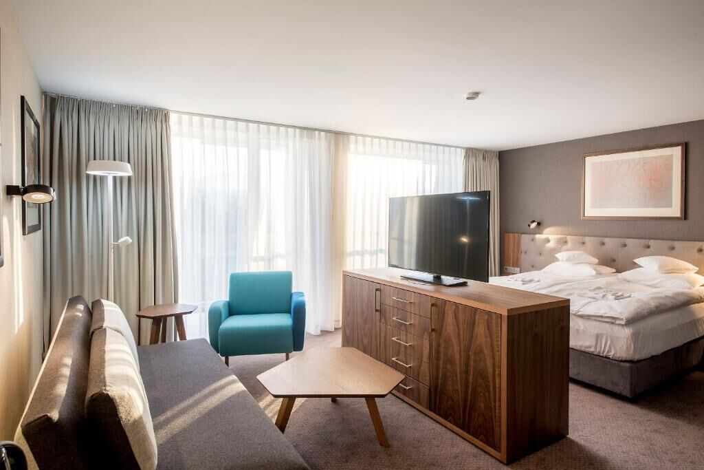 A hotel room with a sofa, a TV on a wooden cabinet, a bed, and a blue chair.