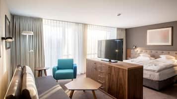 A hotel room with a sofa, a TV on a wooden cabinet, a bed, and a blue chair.