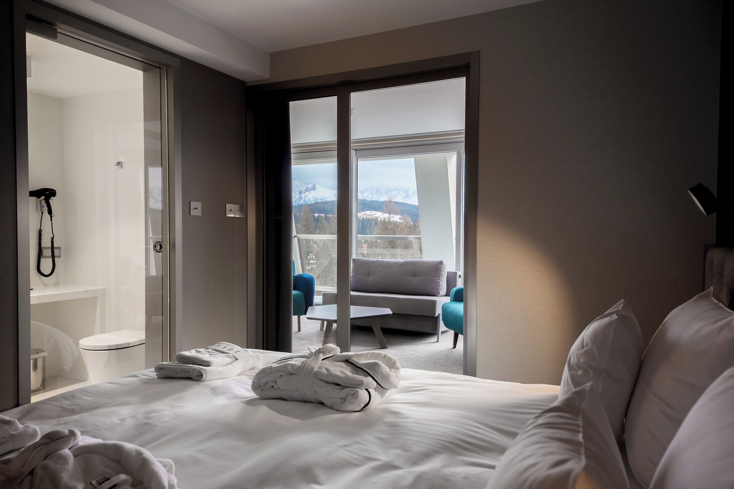 A hotel room with a bed, a bathroom, and a balcony with a view of mountains.