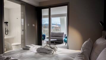 Habitación de hotel con cama, baño y balcón con vistas a montañas.