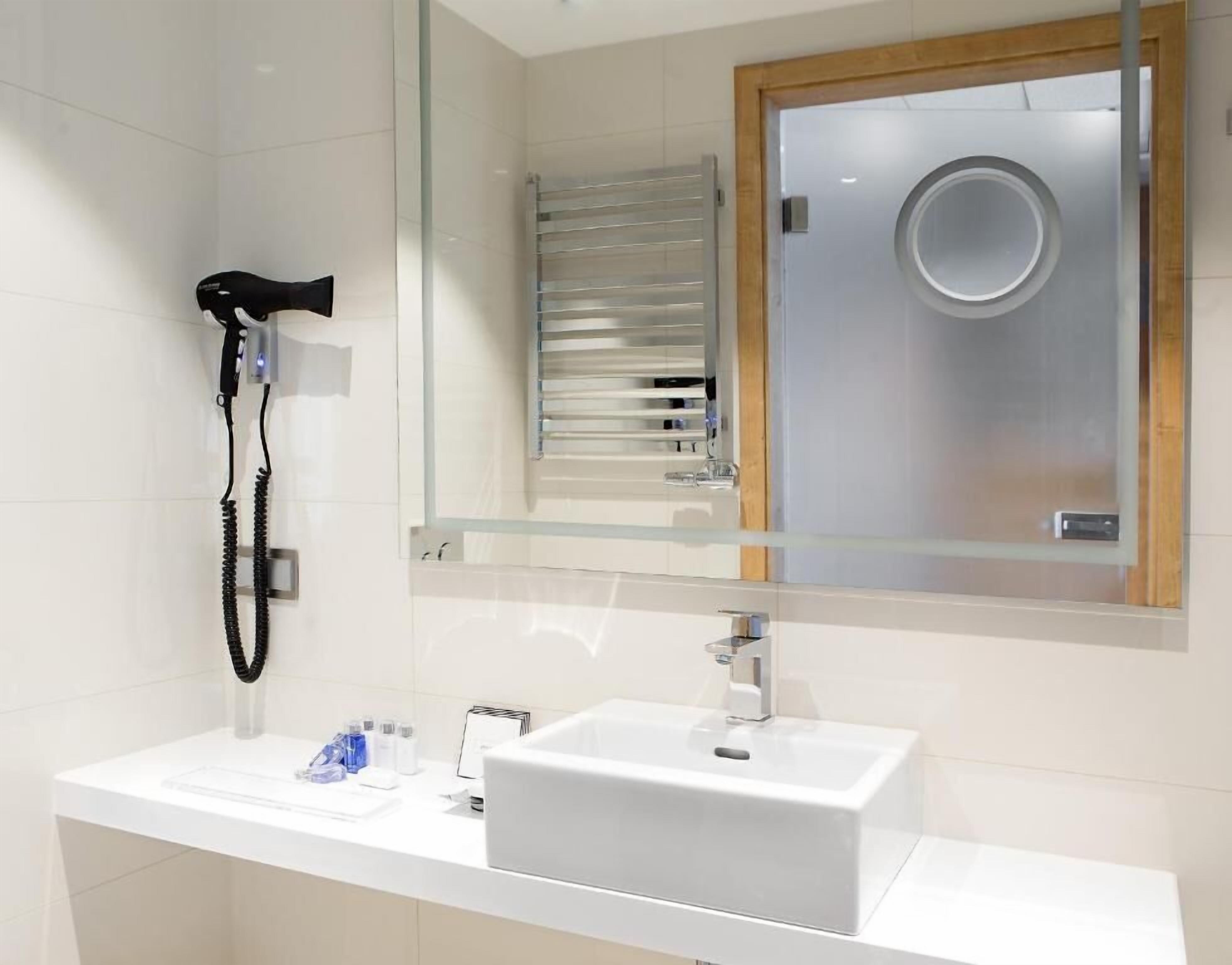 Een badkamer met een wit wastafel, een spiegel, een haardroger en een handdoekhouder.